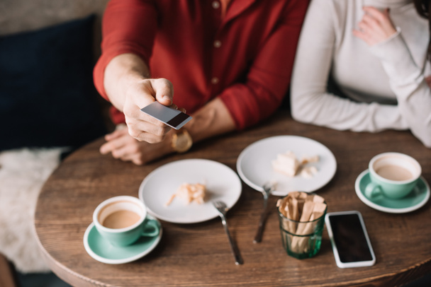 abgeschnittene Ansicht eines jungen Paares, das Käsekuchen isst und Kaffee trinkt, während Mann Kreditkarte im Café hält - Foto, Bild