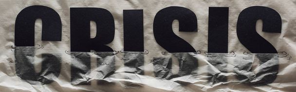 panoramic shot of black word crisis sinking in paper symbolizing water on grey paper background - Photo, image