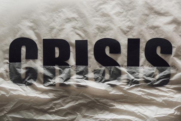  palabra negra crisis inmersa en papel que simboliza el agua sobre fondo de papel gris
 - Foto, Imagen