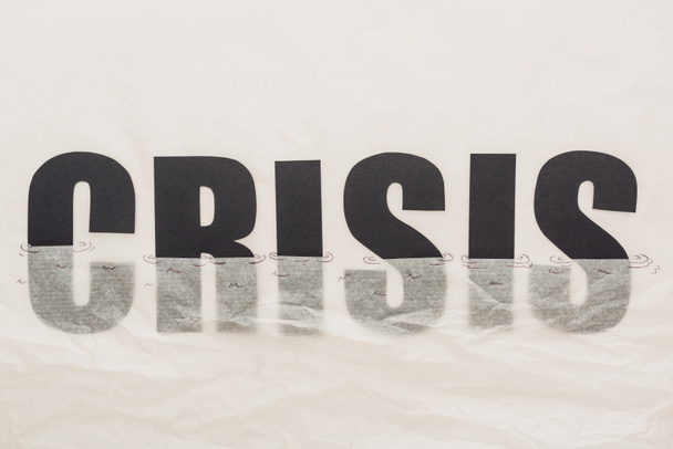 zwart woord crisis ondergedompeld in papier symboliseert water geïsoleerd op wit - Foto, afbeelding