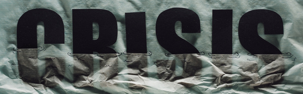 panoramatický záběr černého slova krize ponořen do papíru symbolizující vodu na šedém papíře pozadí - Fotografie, Obrázek