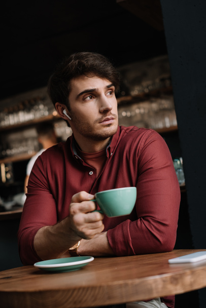 dreamy man in wireless earphones drinking coffee coffee in cafe - Foto, Imagem