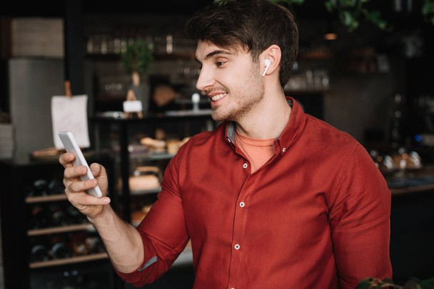 smiling man in wireless earphones using smartphone - Foto, Bild