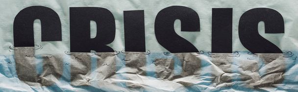 Panoramaaufnahme einer Krise des schwarzen Wortes, die in Papier versinkt und Wasser auf grauem Papier symbolisiert - Foto, Bild