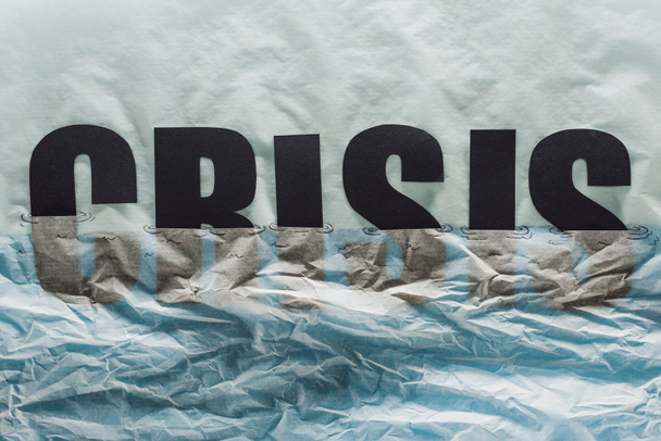 palabra negra crisis inmersa en papel que simboliza el agua sobre fondo de papel gris
 - Foto, Imagen