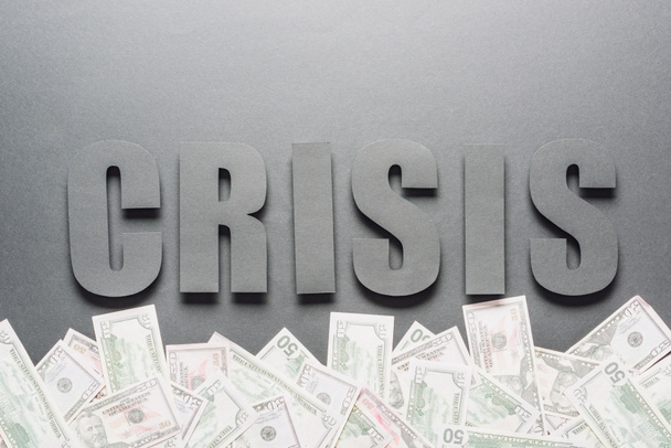 κορυφαία άποψη της κρίσης λέξεων κοντά σε διάσπαρτα τραπεζογραμμάτια δολαρίων σε γκρίζο φόντο με σκιές - Φωτογραφία, εικόνα