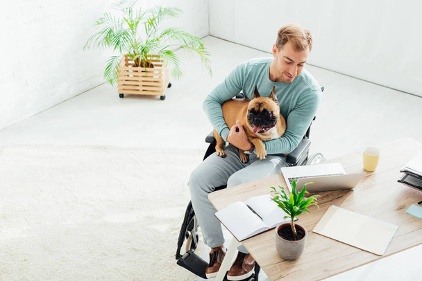 Behinderter mit französischer Bulldogge und Blick auf Laptop im Wohnzimmer - Foto, Bild