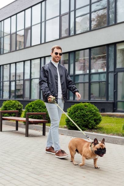 Smiling man walk with french bulldog on leash on urban street - Photo, Image