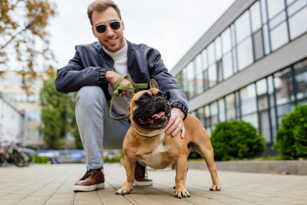 Smiling man holding leash and petting dog on urban street - Фото, зображення