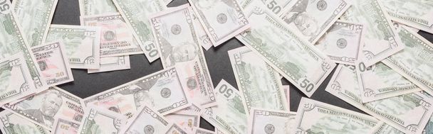bovenaanzicht van verstrooide dollarbankbiljetten op zwarte achtergrond, panoramisch beeld - Foto, afbeelding