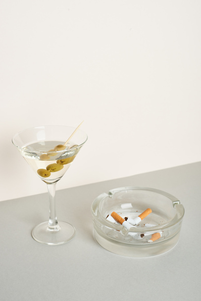 Ashtray with cigarette butts and cocktail on grey surface, isolated on white - Photo, Image