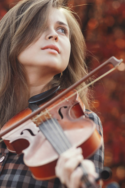 autumn portrait beautiful woman enjoying playing violin on a background of red leaves, romantic girl engaged in art on nature, concept of hobby and music lifestyle - Photo, image