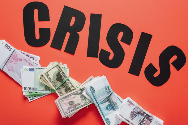 pohled shora na černý papír řez slovo krize na dolar, euro a rubl bankovky na červeném pozadí - Fotografie, Obrázek