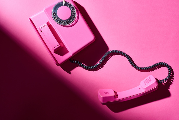 Top view of pink telephone with shadow on bright surface - Zdjęcie, obraz