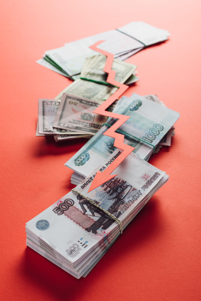 selectieve focus van papier gesneden recessie pijl op roebel, dollar en eurobankbiljetten op rode achtergrond - Foto, afbeelding