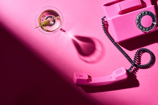 Top view of glass with martini and retro telephone on pink background - Photo, Image