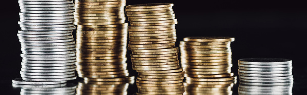 panoramic shot of stacked silver and golden coins on surface with reflection isolated on black - Foto, afbeelding