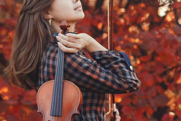 young woman with red violin and and bow on a background of autumn nature, romantic girl engaged in musical art, a concept of hobby, concert outdoors - Foto, Imagem