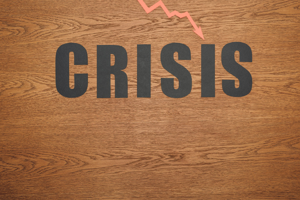 bovenaanzicht van zwart papier gesneden woord crisis en recessie pijl op houten oppervlak met kopieerruimte - Foto, afbeelding