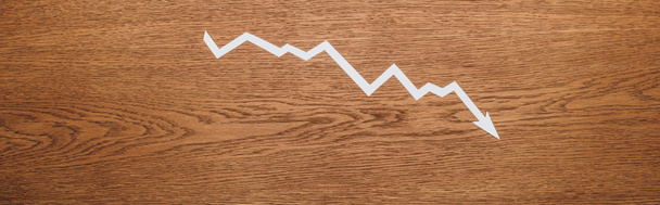 Draufsicht auf weißen Papierschnitt Rezessionspfeil auf Holzschreibtisch, Panoramaaufnahme - Foto, Bild