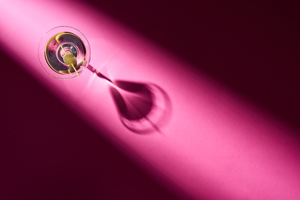 Bovenaanzicht van martini met olijf op roze achtergrond met schaduw - Foto, afbeelding
