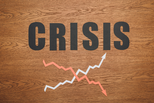 bovenaanzicht van zwart papier gesneden woord crisis in de buurt van toename en recessie pijlen op houten bureau - Foto, afbeelding
