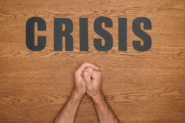 обрезанный вид мужских сложенных рук рядом с черной бумагой вырезать слово кризис на деревянном столе
 - Фото, изображение
