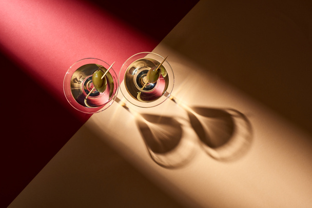 Top view of cocktails with olives with shadows on red and beige background - Foto, Bild