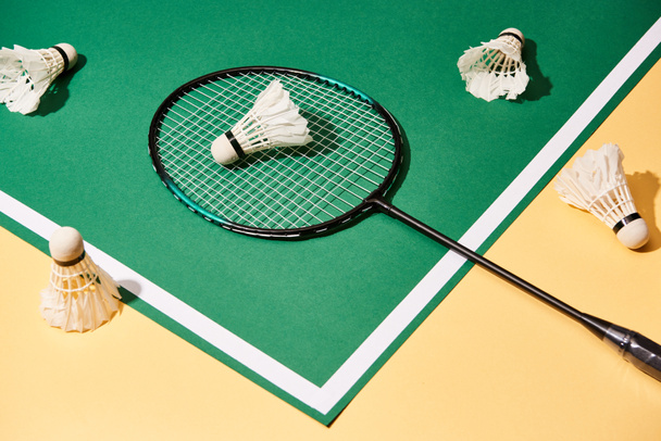 Yüksek açılı badminton raketi ve yeşil ve sarı arka planda mekik penisleri - Fotoğraf, Görsel