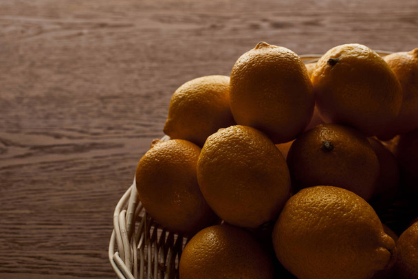 ripe yellow whole lemons in wicker basket on wooden background - Photo, Image