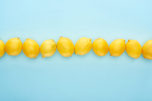 flat lay with ripe yellow lemons in line on blue background - Zdjęcie, obraz