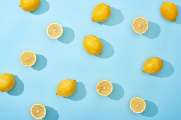 top view of whole and cut yellow lemons on blue background - Fotó, kép