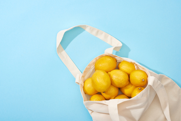 top view of ripe yellow lemons in cotton eco bag on blue background - Fotó, kép