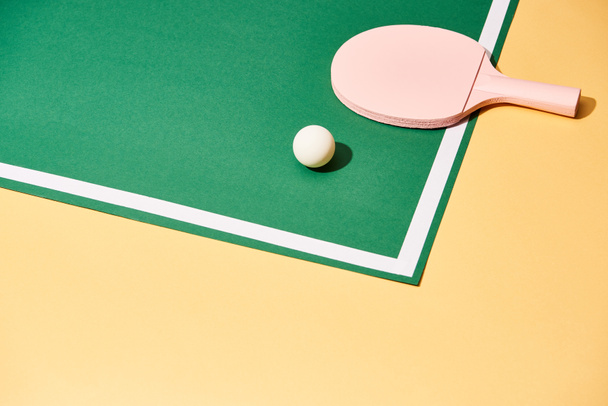 Ράκετ και μπάλα για πινγκ πονγκ στο τραπέζι σε κίτρινο φόντο - Φωτογραφία, εικόνα