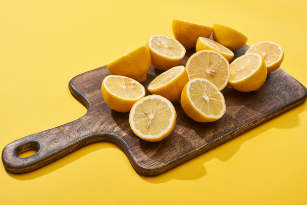 ripe cut lemons on wooden cutting board on yellow background - Foto, Imagem