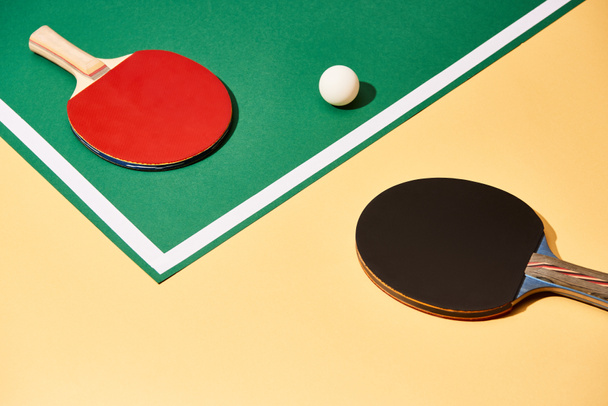 Two table tennis rackets and ball on green and yellow surface with white line - Photo, Image