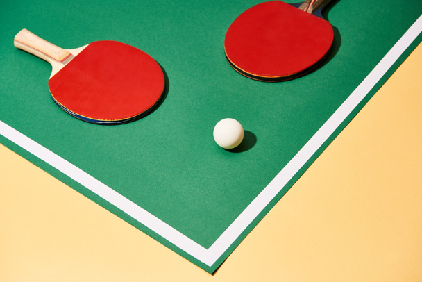 Red table tennis rackets and ball on green and yellow surface  - Фото, изображение