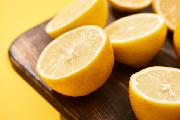 close up view of ripe cut lemons on wooden cutting board on yellow background - Foto, afbeelding