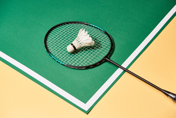 Metal badminton racket and shuttlecock on green and yellow surface with line - Fotó, kép
