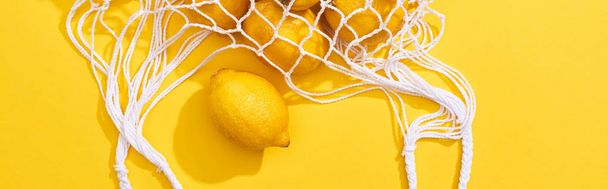 верхний вид свежих спелых целых лимонов в эко-мешок струны на желтом фоне, панорамный снимок
 - Фото, изображение