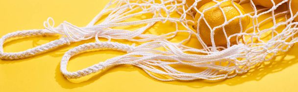 limões inteiros maduros frescos no saco de corda ecológica no fundo amarelo, tiro panorâmico
 - Foto, Imagem