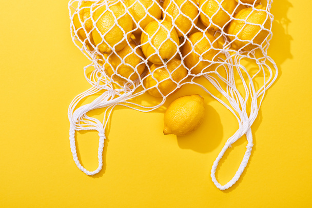 top view of fresh ripe whole lemons in eco string bag on yellow background - Photo, Image