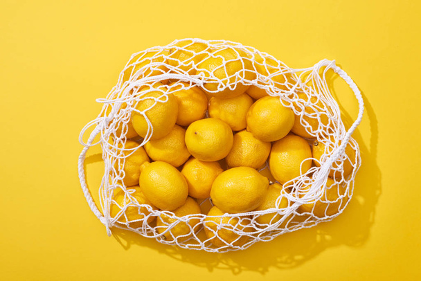 top view of fresh ripe whole lemons in eco string bag on yellow background - Foto, afbeelding