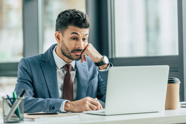 surprised businessman looking at laptop while sitting at workplace - Foto, Imagem