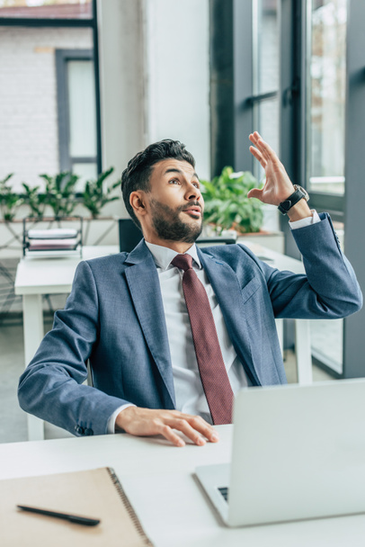 excited businessman showing idea gesture while sitting at workplace and looking up - Foto, imagen