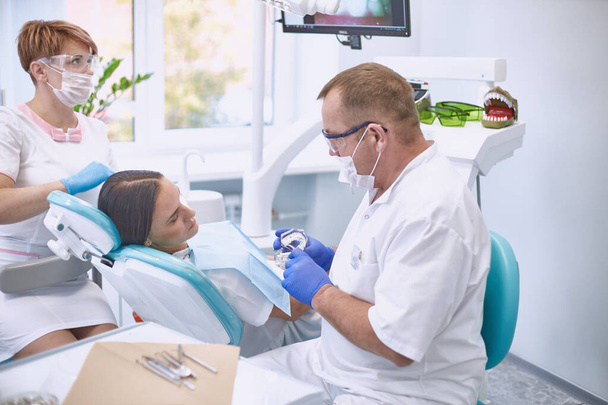 Doktor zubař léčí zuby krásné mladé dívky pacienta. Ta dívka na recepci u zubaře. Zubař ošetřuje zub - Fotografie, Obrázek