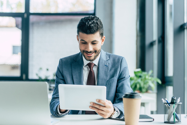 hombre de negocios alegre usando tableta digital mientras está sentado en el lugar de trabajo
 - Foto, imagen