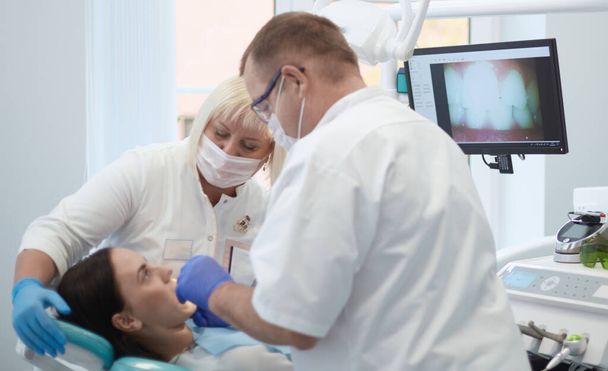 Γιατρός οδοντίατρος αντιμετωπίζει τα δόντια ενός όμορφου ασθενή νεαρή κοπέλα. Το κορίτσι στη ρεσεψιόν στον οδοντίατρο. Γιατρός οδοντίατρος αντιμετωπίζει δόντι - Φωτογραφία, εικόνα