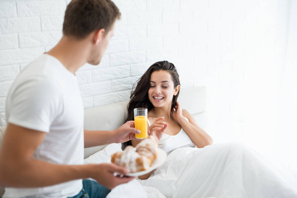 young man prepared breakfast - croissants and orange juice in bed for his beloved wife looking happy morning family idyll - Zdjęcie, obraz