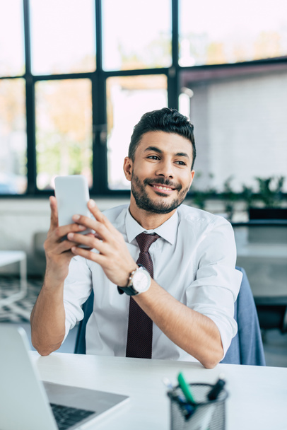 selective focus of cheerful businessman looking away while holding smartphone - Photo, Image